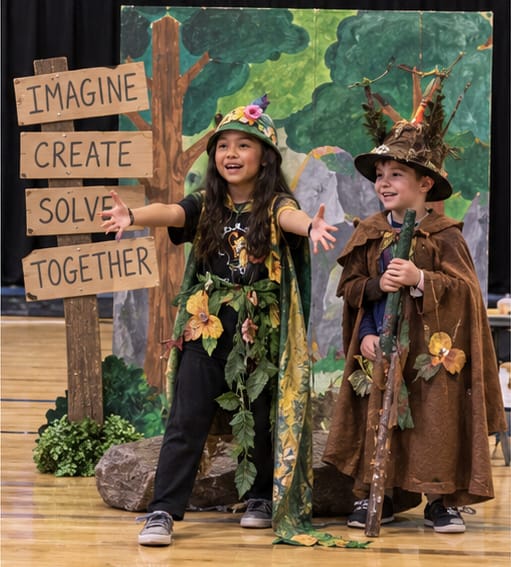 Two students in forest costumes performing in front of a painted tree backdrop